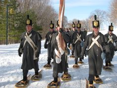 a group of men in uniforms on skis walking through the snow with flags attached to their heads