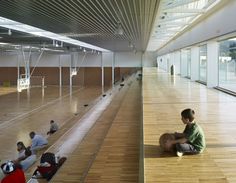 there are many people sitting on the floor in an empty room with wood floors and glass walls