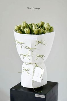 a bouquet of flowers in a white paper bag on top of a black box with a tag tied to it