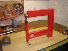 a red machine sitting on top of a wooden table next to a wall with pictures behind it