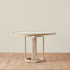 a round table with a glass top on a wooden floor in front of a white wall