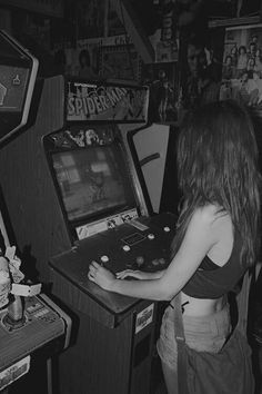 a woman playing an arcade game in a room with posters on the wall behind her