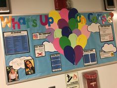 a bulletin board with balloons attached to the wall and writing on it that says what's up