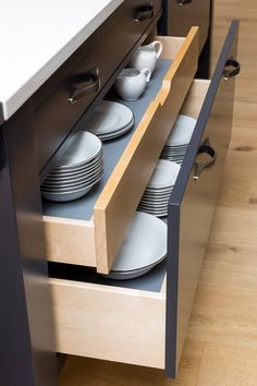 an open drawer with plates and cups in it on a wooden floor next to a counter