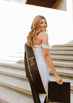 a woman in a black and white graduation gown is walking down the stairs with her diploma