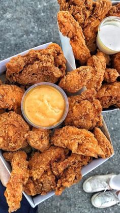 a person holding a box filled with fried chicken and dipping sauce