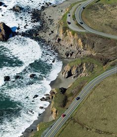 an aerial view of the ocean and coastline with cars driving on road next to it