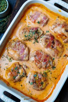 a casserole dish with meat covered in sauce and garnished with herbs