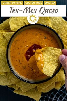 a hand holding a tortilla chip over a bowl of tex - mex queso