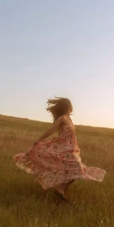 a woman in a dress is running through the grass with her hair blowing in the wind