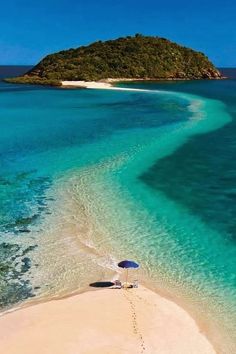 an island in the middle of blue water next to white sand beach with umbrellas on it