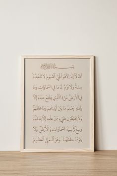 an arabic text is framed in a white frame on a wooden shelf next to a wall