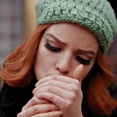 a woman with red hair wearing a green crochet hat and holding her hand to her mouth