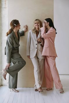 three women standing next to each other in front of a wall with their hands together