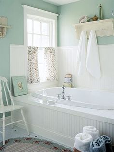 a white bath tub sitting under a window next to a chair in a room with blue walls