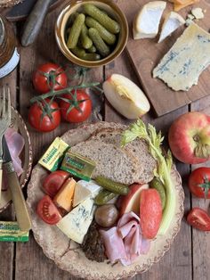 an assortment of cheese, meats and vegetables on a wooden table next to other food items