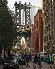 many people are walking on the sidewalk in front of some tall buildings and a bridge