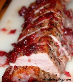 meat covered in cranberry sauce sitting on top of a cutting board