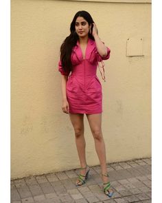 a woman in a pink dress is talking on her cell phone while standing next to a wall