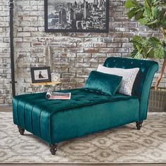 a green velvet chaise lounge in front of a brick wall and potted plant