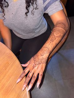 a woman sitting at a table with henna tattoos on her arm and hand,