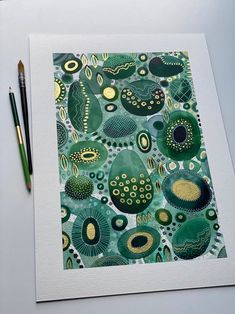 a painting with green and gold designs on it, next to a pen and paper