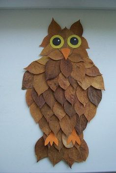 an owl made out of leaves sitting on top of a white surface with yellow eyes