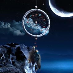 a dream catcher hanging from the side of a cliff in front of a crescent moon