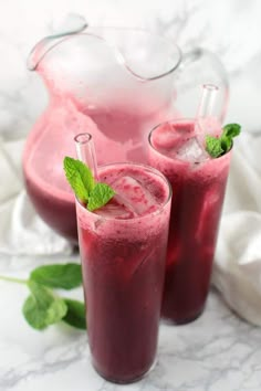 two glasses filled with pink liquid and mint garnish next to a pitcher on a marble table