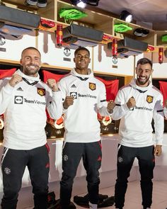 three men standing next to each other in front of red and white soccer jerseys holding trophies