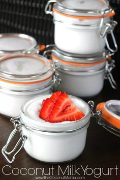 four small jars with strawberries in them on a table next to some spoons