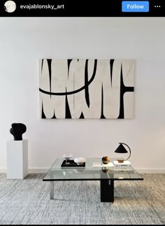 a glass table in front of a white wall with black and white artwork on it