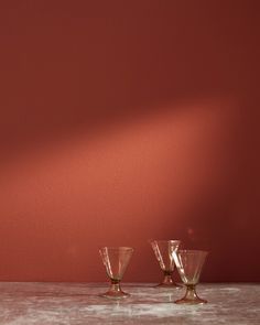 three wine glasses sitting on top of a table next to a red wall and floor