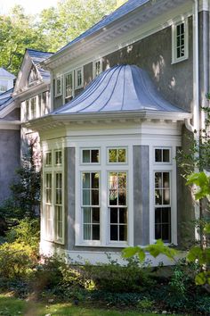 a house with white windows and a blue tin roof on the side of it, surrounded by greenery