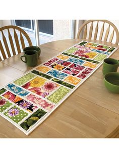 the table runner is decorated with colorful flowers and green mugs on top of it