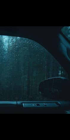 the inside of a car with rain drops on the windshield and trees in the background