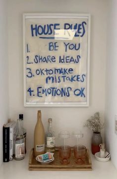 a wooden tray topped with glasses next to a framed sign that reads house rules i be you