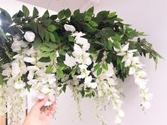 a person is holding flowers in front of a white wall with green leaves on it