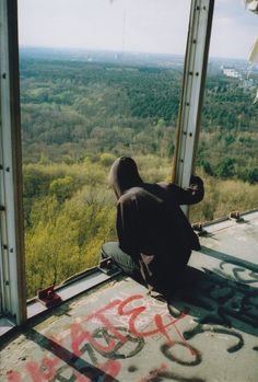 a man sitting on top of a tall building next to a window covered in graffiti