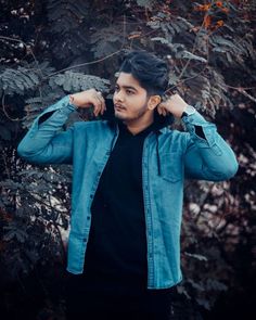 a man standing in front of a tree with his hands on his ears and looking off to the side