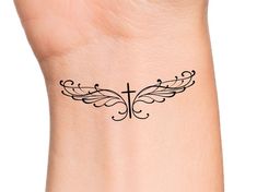 a cross with wings tattoo on the side of a woman's wrist and hand