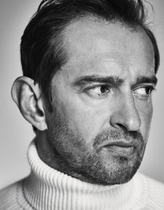 a black and white photo of a man in a turtle neck sweater looking at the camera