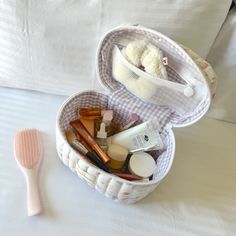 a white basket filled with cosmetics and a pink toothbrush sitting on top of a bed