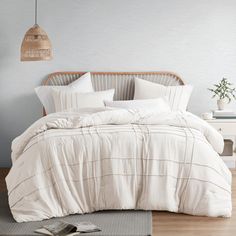 a bed with white linens and pillows in a room next to a lamp on the wall