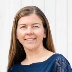 a woman standing in front of a white wall smiling at the camera with her hands on her hips