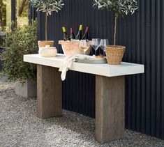 an outdoor table with two olive trees on it and wine bottles in the middle next to it