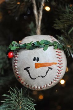 a baseball ornament hanging on a christmas tree with lights in the background and snowman's face painted on it