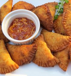 several pastries on a plate with sauce in a bowl next to it and garnishes