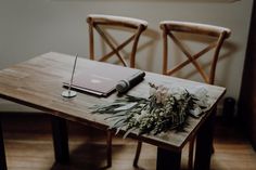 a wooden table topped with a laptop computer next to a bouquet of flowers on top of it