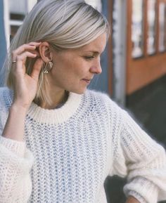 a woman with blonde hair is talking on her cell phone and wearing a white sweater